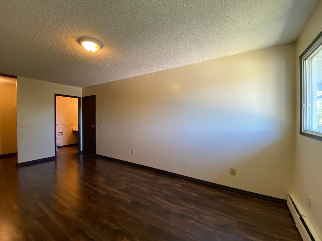 A room with wooden floors and a window on the right side.