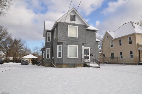 A grey house with a white roof and a snow-covered ground.