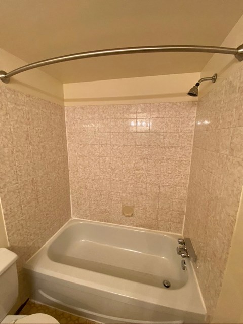 A white bathtub in a bathroom with a toilet and a shower head.