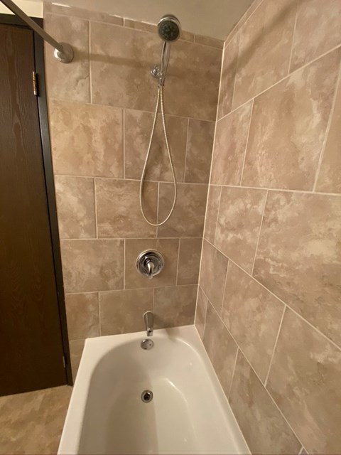 A white bathtub with a shower head and hand held shower.
