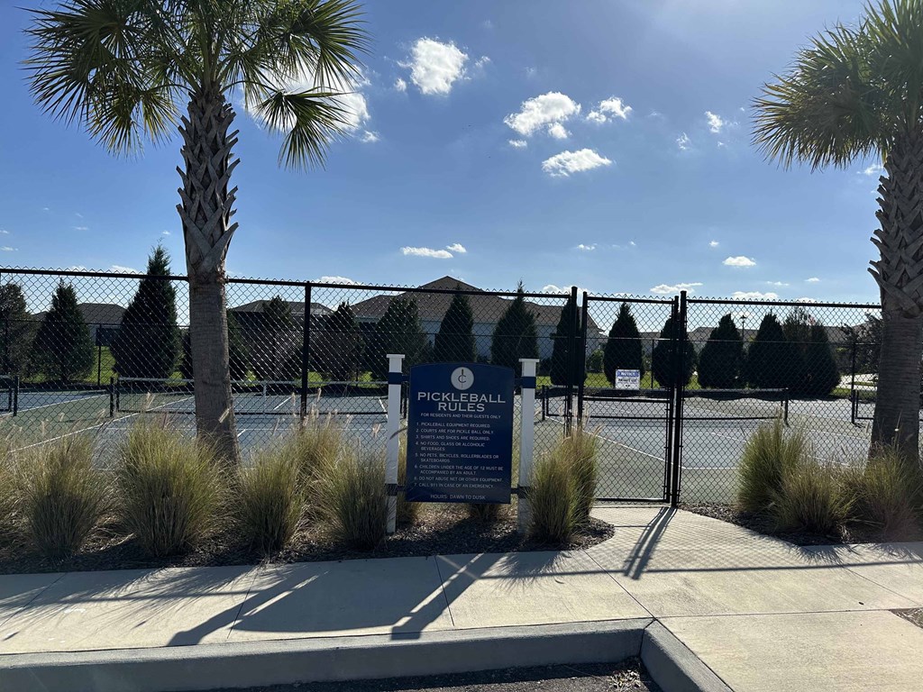 a sign in front of a tennis court with palm trees