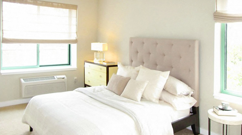 a bedroom with a bed and pillows and two windows