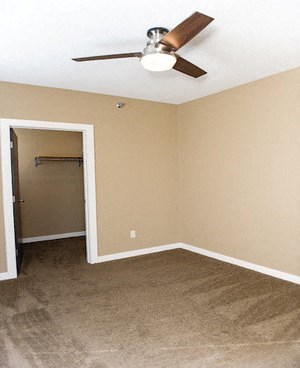 an empty living room with a ceiling fan and a closet