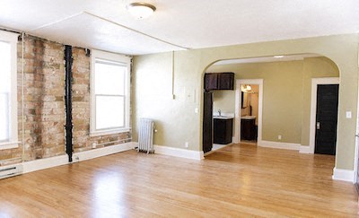 an empty living room with a wood floor and a brick wall