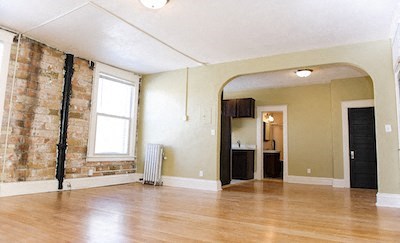an empty living room with a wood floor and an exposed brick wall