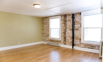 an empty living room with a wood floor and a brick wall