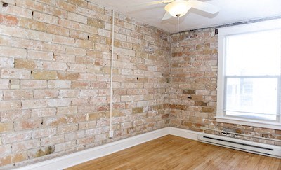 an empty room with an exposed brick wall and a ceiling fan