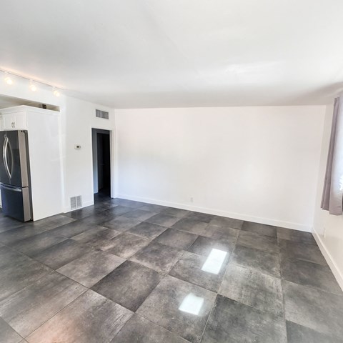 an empty living room with white walls and a stainless steel refrigerator