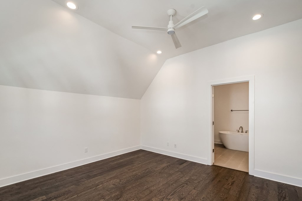 a living room with white walls and a wooden floor and a ceiling fan