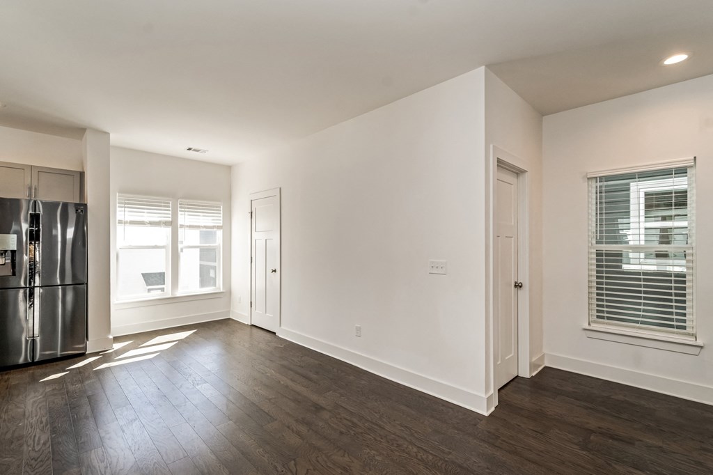 an empty living room with white walls and a stainless steel refrigerator