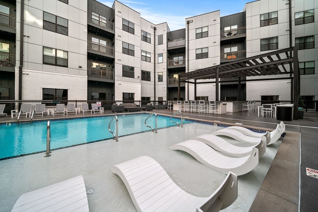 a swimming pool with white lounge chairs in front of buildings