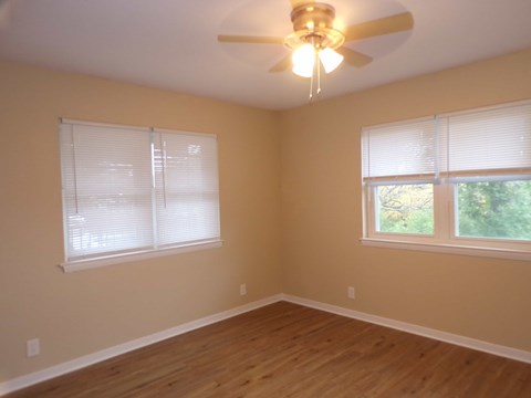 A room with a ceiling fan and two windows.