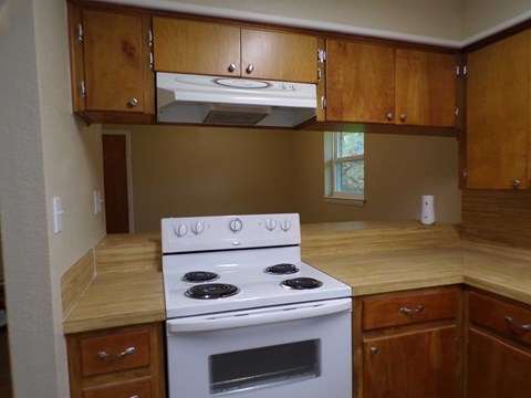 A white stove with four burners is in a kitchen with wooden cabinets.