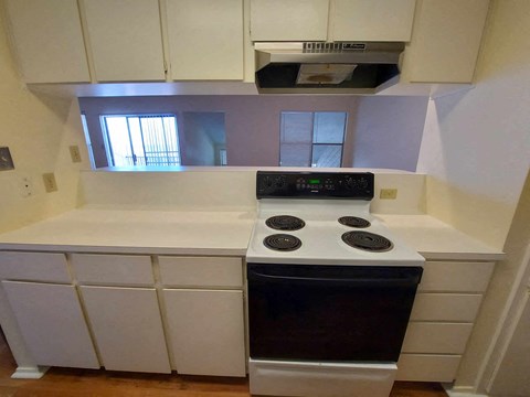 A white kitchen with a stove top oven and a window.