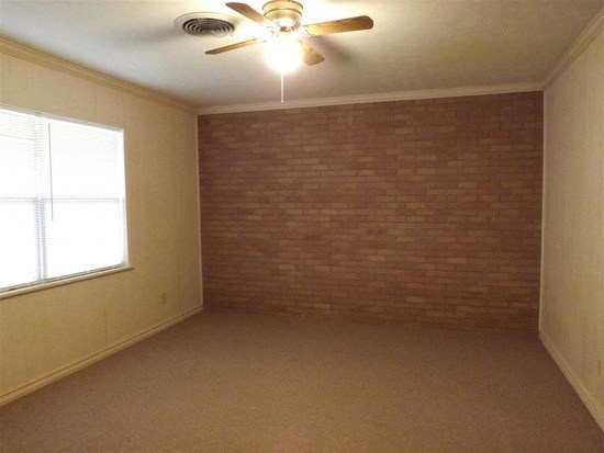 an empty room with a ceiling fan and a brick wall