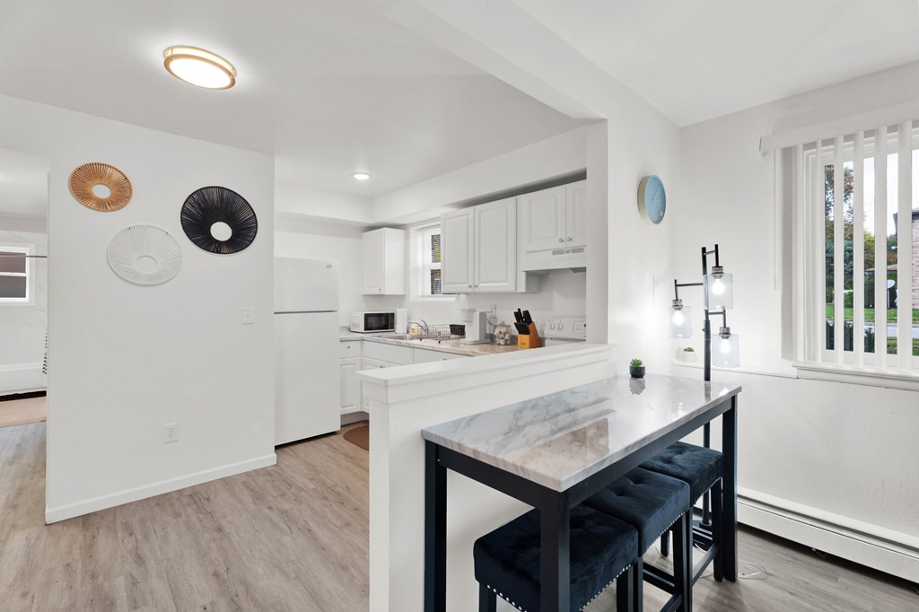 A kitchen with a table and chairs in the foreground and a white refrigerator in the background.