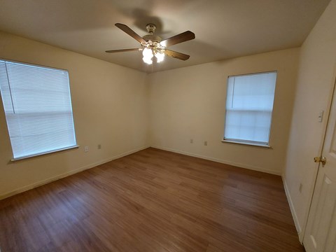 A room with a ceiling fan and two windows.