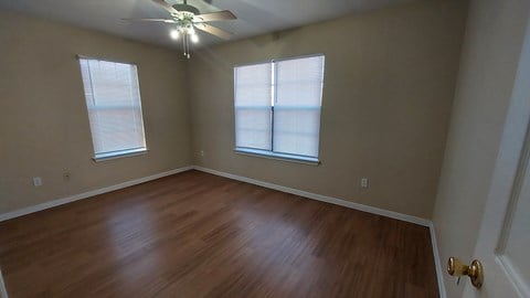 A room with a ceiling fan and two windows.