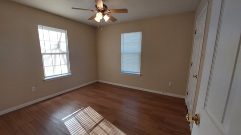 A room with a ceiling fan and two windows.