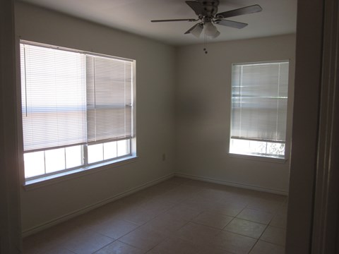an empty living room with two windows and a ceiling fan