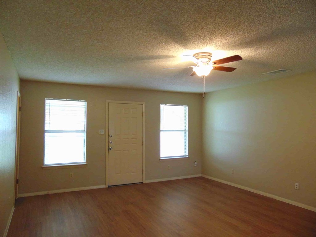 an empty living room with a ceiling fan and a door