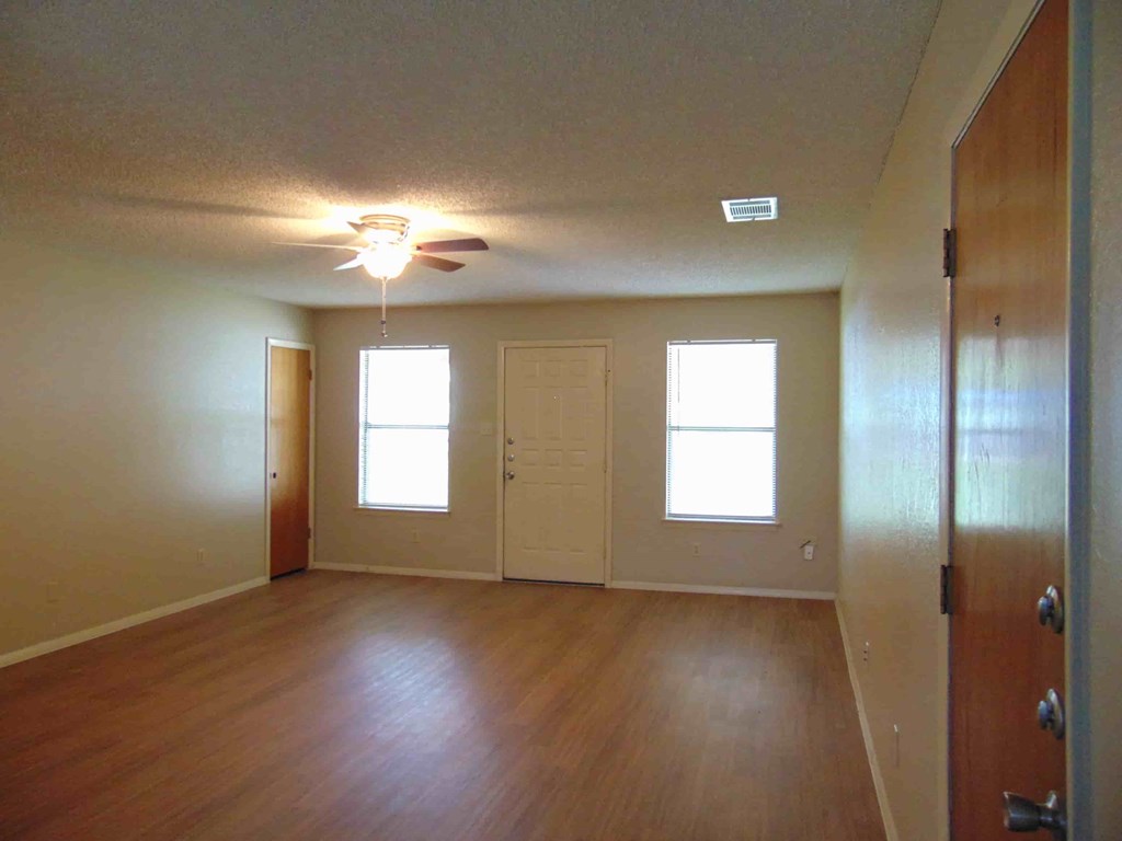 an empty living room with wood floors and a ceiling fan