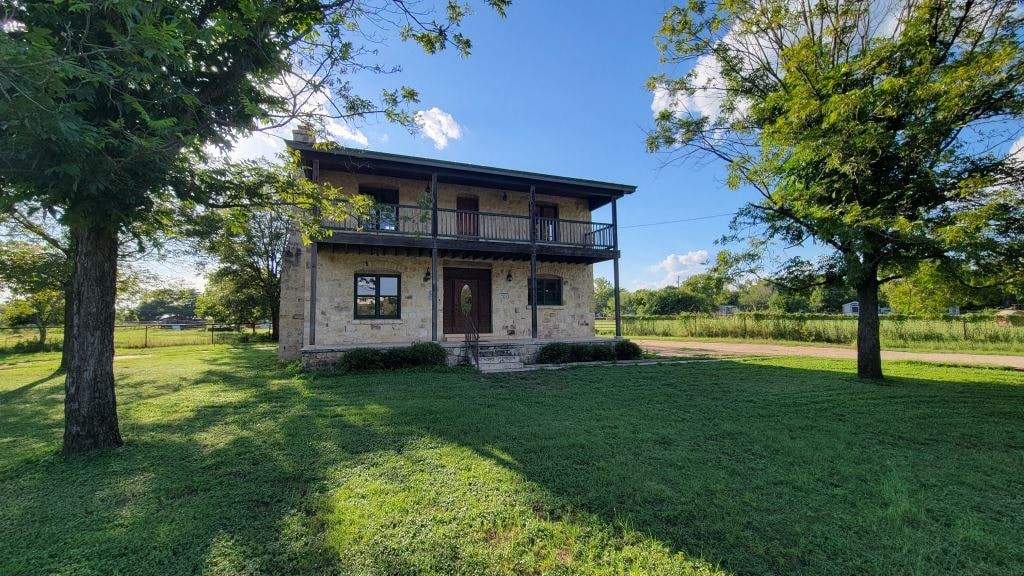a stone house with a yard and trees in front of it