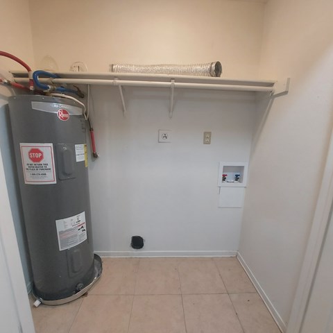 A room with a water heater and a white shelf above it.