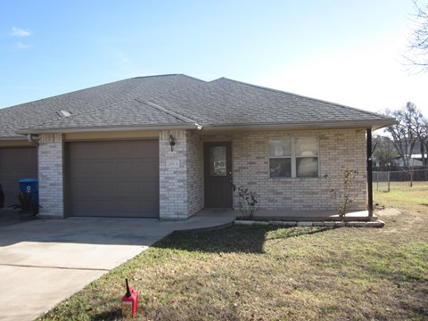 A house with a grey garage door and a small tree in front.