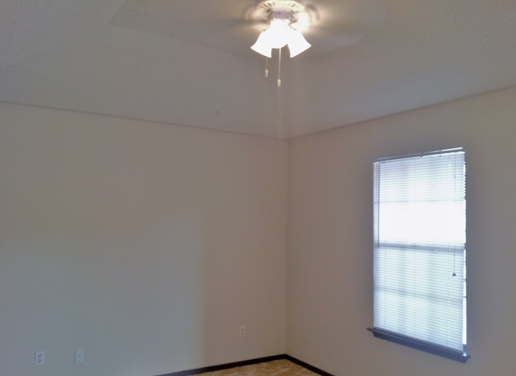 the corner of a room with a ceiling fan and a window