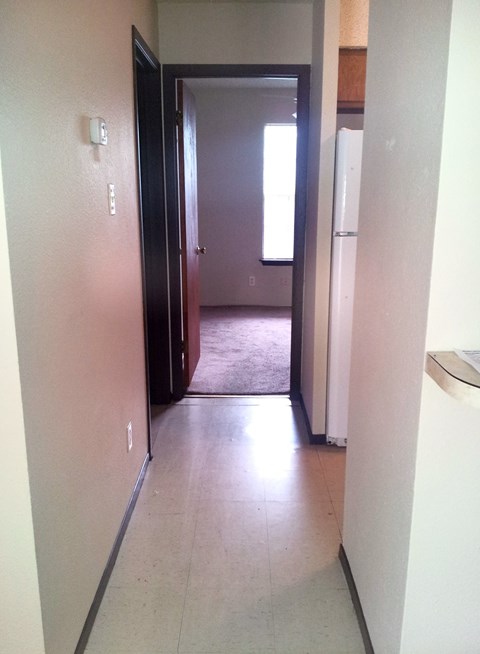 A hallway with a door on the left and a refrigerator on the right.