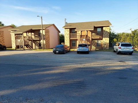 A parking lot with two cars and two houses in the background.