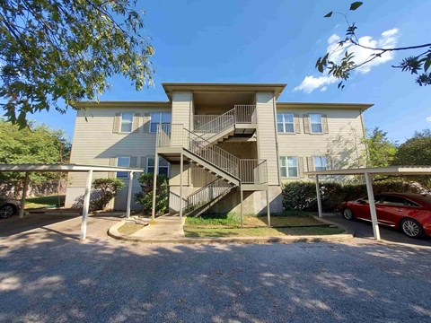 A two-story residential building with a red car parked in front.