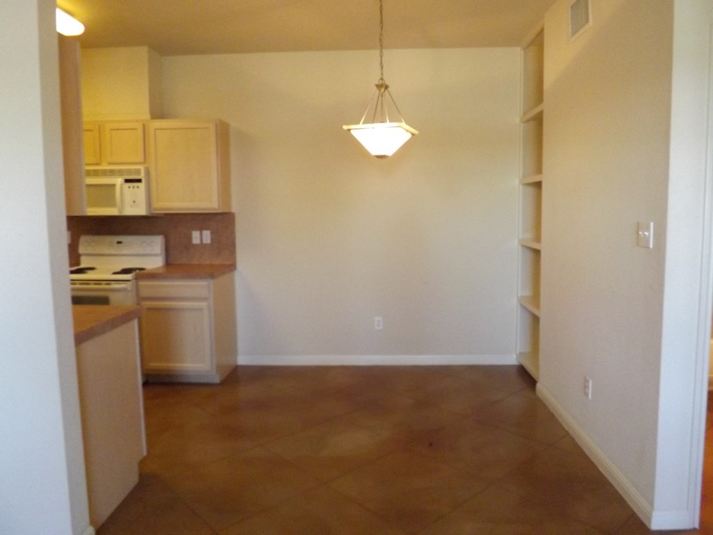 an empty living room with a kitchen and a lamp