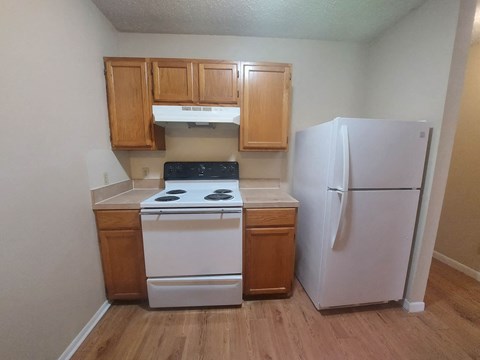 A small kitchen with a white refrigerator, white stove, and wooden cabinets.