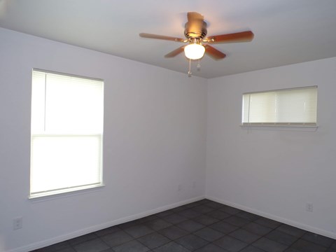 A room with a ceiling fan and two windows.