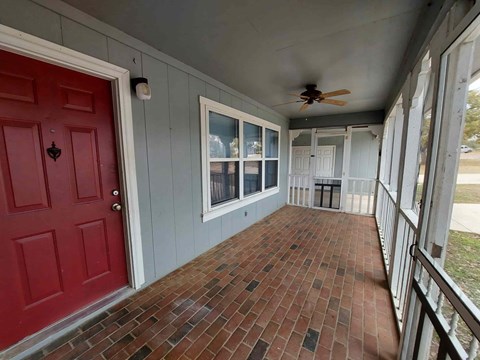 A red door is on the left of a porch with a ceiling fan.