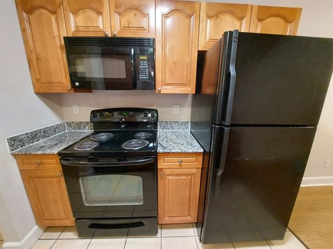 A black refrigerator stands next to a black microwave and oven in a kitchen.