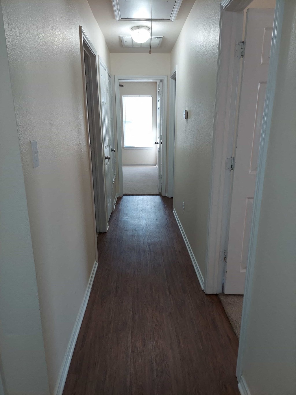 a hallway with a wood floor and white walls and a window