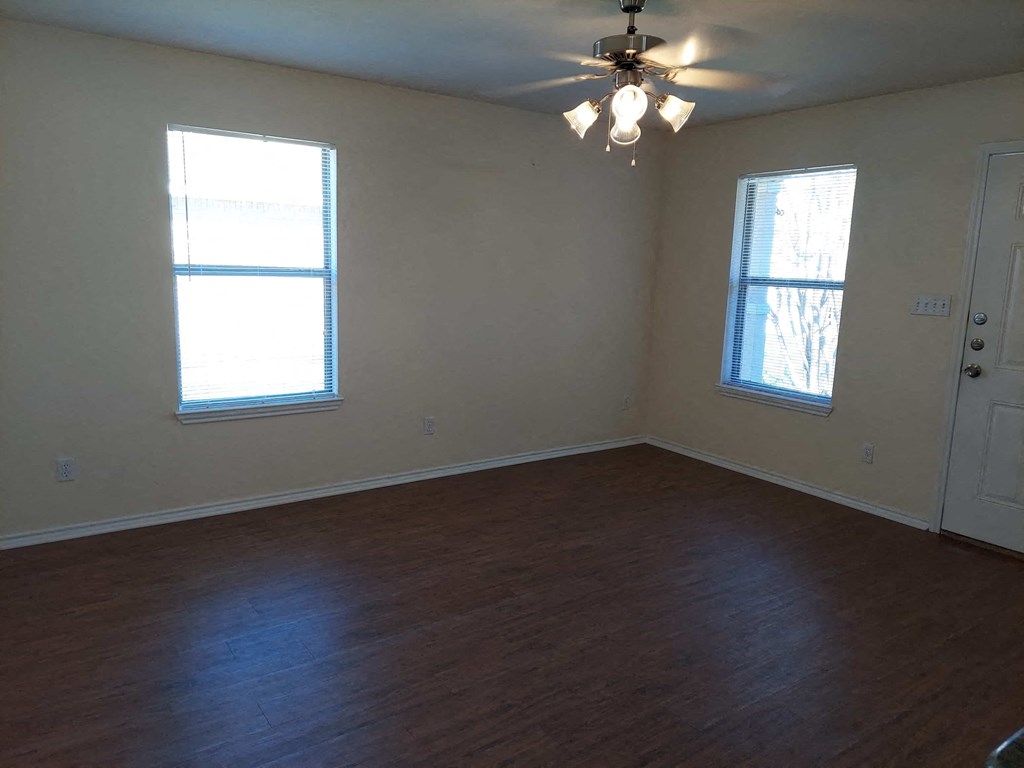 an empty living room with a ceiling fan and two windows