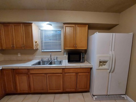 A white refrigerator stands next to a kitchen sink.