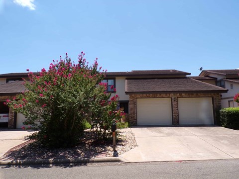 A house with a brown roof and a tree with pink flowers in front.