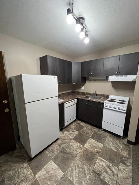 A kitchen with a white refrigerator, black cabinets, and a tiled floor.
