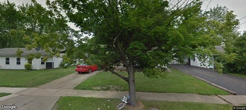 a red car driving down a street next to a tree