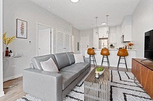 A grey couch with a white pillow is in the middle of a room with a black and white rug.