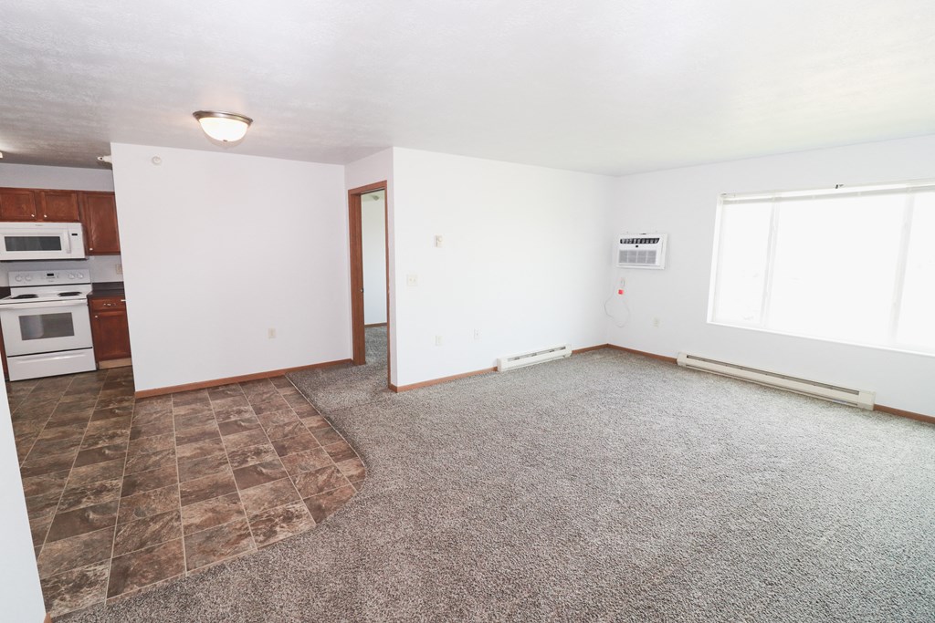 an empty living room with carpet and a kitchen