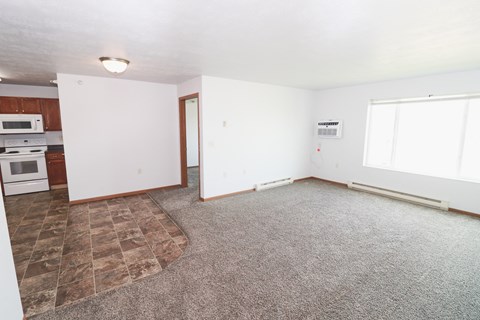 an empty living room with carpet and a kitchen