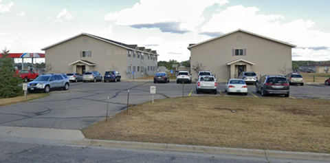 A parking lot with cars parked in front of two buildings.