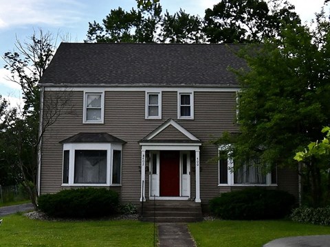 a brown house with a red door on a lawn