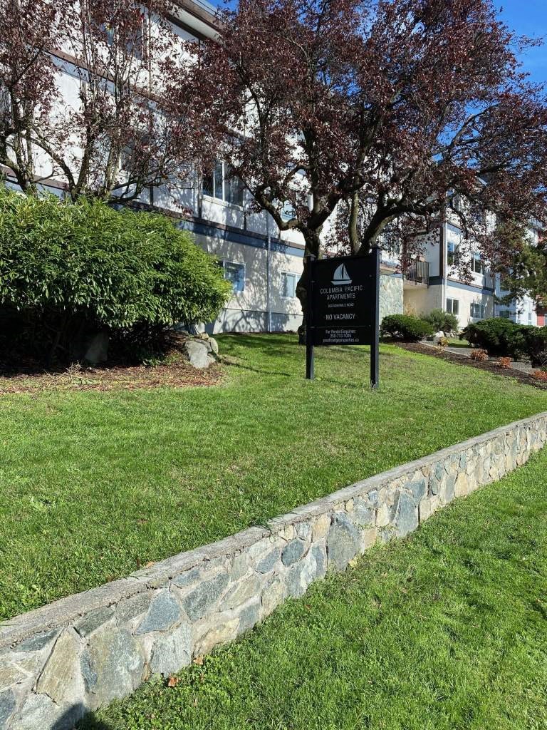 a black sign in the grass in front of a building